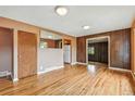 Spacious room featuring hardwood floors, wood paneling, and a door leading to the kitchen at 380 E 111Th Pl, Northglenn, CO 80233