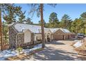 A beautiful exterior view, with a stone finish and a three-car garage, all surrounded by natural forest and light snow at 24860 N Mountain Park Dr, Evergreen, CO 80439
