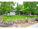 Attractive home featuring a stone retaining wall, lush landscaping, a well-maintained lawn, and white painted brick at 3125 Xenon St, Wheat Ridge, CO 80215