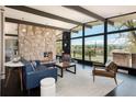 Bright living room featuring a stone fireplace, dark wood floors and beams, and a wall of windows with outdoor views at 8 Lindenwood Dr, Littleton, CO 80120