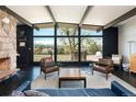An airy living room with a stone fireplace, expansive windows and a view of trees and a deck at 8 Lindenwood Dr, Littleton, CO 80120