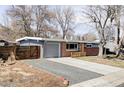 Inviting single-story home with a brick and gray facade, attached garage, and a gravel driveway bordered by brick edging at 5945 Dudley Ct, Arvada, CO 80004