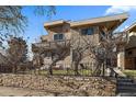 Elegant home showcasing stone accents and a second story balcony, framed by a stone wall and lush greenery at 3323 W Hayward Pl, Denver, CO 80211