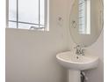 Stylish half-bathroom with pedestal sink, round mirror, and natural light from the window at 7260 Waterleaf Trl, Littleton, CO 80125