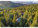 Aerial view showcases the secluded property surrounded by a dense forest and stunning mountain views in the background at 34100 Woodland Dr, Evergreen, CO 80439