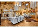 Open-concept living room featuring a stone fireplace, log walls, high ceilings, and a spacious dining area with hardwood floors at 34100 Woodland Dr, Evergreen, CO 80439