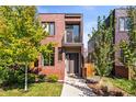 Modern brick home features a small balcony and lush landscaping around the front yard and walkway in a vibrant neighborhood at 1833 E Jewell Ave, Denver, CO 80210