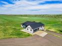 Aerial view of a modern farmhouse with a three-car garage and large driveway in a green field at 2400 Ventress Ct, Bennett, CO 80102
