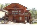 Unique cabin with a balcony, wooden details, and swing sets, set against a tree-lined backdrop at 9705 Canon Dr, Sedalia, CO 80135