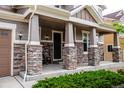 Inviting porch with stone pillars, dark front door, and a seating area for relaxing outdoors at 3421 E 143Rd Dr, Thornton, CO 80602