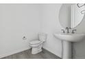Modern powder room with a pedestal sink, round mirror, updated fixtures, and a white toilet at 25234 E Warren Pl, Aurora, CO 80018