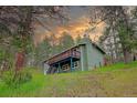 Charming two-story home with a spacious deck on a green hillside surrounded by mature trees at sunset at 5237 S Olive Rd, Evergreen, CO 80439