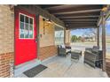 Inviting covered front porch with seating area, bright red door, and brick accents at 7624 Navajo St, Denver, CO 80221