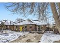 Brick Ranch home with yellow door, snowy yard, and mature trees at 543 S Bryant St, Denver, CO 80219