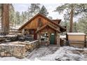 Charming wood and stone cabin with snow-covered roof and patio in a serene wooded setting at 26288 S End Rd, Kittredge, CO 80457