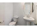 Modern powder room with a pedestal sink, toilet, and round mirror at 455 S Salida St, Aurora, CO 80017