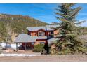 Charming two-story home with a wood exterior, gray roof, porch, and mature trees against a mountain backdrop at 31299 Manitoba Dr, Evergreen, CO 80439