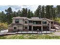 Expansive tan stucco home with stone accents, large windows, and a spacious patio area in a wooded setting at 1988 Lake Dr, Larkspur, CO 80118