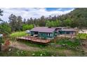 Inviting home with a large wooden deck, surrounded by lush greenery and mature trees at 8537 S Doubleheader Hwy, Morrison, CO 80465