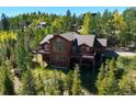 Stunning aerial view of wood cabin surrounded by trees, showcasing large windows and an expansive deck at 10333 Georgia Cir, Morrison, CO 80465