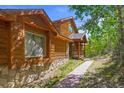 Beautiful wood cabin with stone accents, large windows, and a sidewalk, surrounded by a lush forest at 10333 Georgia Cir, Morrison, CO 80465