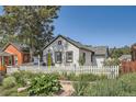 Charming cottage featuring a yellow door, white picket fence, and lush front garden at 4883 Perry St, Denver, CO 80212