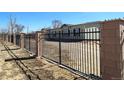 View of property behind a decorative iron fence with brick columns and a gravel driveway at 15460 Casler Ave, Fort Lupton, CO 80136