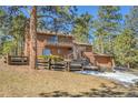 Two story home surrounded by a wooden fence and tall trees with an elevated deck and partial driveway view at 29571 Dorothy Rd, Evergreen, CO 80439