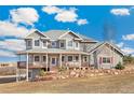 Beautiful two-story home featuring a spacious wrap-around porch, enhanced by a stone retaining wall and mature trees at 931 Forest View Rd, Monument, CO 80132
