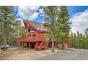 Red cabin home with a large deck nestled among the trees in a mountain setting at 387 Pine Dr, Idaho Springs, CO 80452