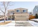 Two-story house with beige exterior, attached garage, and snowy landscape at 11002 Glacier Park Cir, Parker, CO 80138