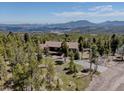 Stunning aerial view of a home surrounded by a lush forest with views of the mountains in the distance at 32091 Black Widow Dr, Conifer, CO 80433