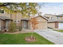 Tan two-story townhome with attached garage, landscaping, and a tree at 9673 Ironton St, Commerce City, CO 80022