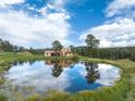 Scenic tan two-story home and trees reflecting in a pond on a beautiful day at 28098 Green Valley Ln, Conifer, CO 80433
