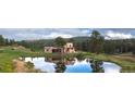 Scenic view of tan two-story home, trees, and pond with mountain views on a sunny day at 28098 Green Valley Ln, Conifer, CO 80433