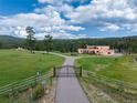 Tan two-story home with a gated entrance and long driveway nestled in the mountains at 28098 Green Valley Ln, Conifer, CO 80433