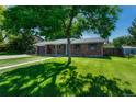 A single-Gathering brick house boasting a lush green lawn, framed by mature trees and a clear, sunny sky at 7479 Pierce St, Arvada, CO 80003
