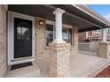 A close-up of a covered front porch with brick pillars, a black front door, and recessed lighting at 9250 Roadrunner Dr, Highlands Ranch, CO 80129