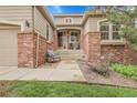 Inviting front porch with red brick accents and a gray chair at 1033 Bramblewood Dr, Castle Pines, CO 80108