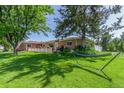 Serene backyard featuring lush green lawn, mature trees providing shade, and a relaxing hammock at 17450 E 14Th Dr, Aurora, CO 80011