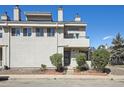 View of a townhouse with neutral stucco exterior, mature landscaping, and a private balcony on the second floor at 1830 Newland Ct # 101, Lakewood, CO 80214