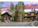 A luxurious stone and wood home with a circular driveway is framed by a vibrant sunset sky at 215 Royal Tiger Rd, Breckenridge, CO 80424