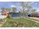 Charming single-story home with blue siding, red door, and driveway with carport surrounded by lush greenery at 41 Cortez St, Denver, CO 80221
