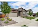 Street view of a charming home featuring a well-manicured lawn, a two-car garage, and stone accents at 5771 Slate River Pl, Brighton, CO 80601