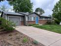 Single-story home featuring a gray exterior, brick accents, a blue front door, and a long driveway at 18908 E Napa Dr, Aurora, CO 80013