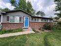Front view of a home featuring gray siding, brick accents, a blue front door, and green landscaping at 18908 E Napa Dr, Aurora, CO 80013