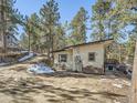 Quaint house surrounded by trees, boasting a cozy patio area and practical wood storage near the entrance at 28251 Meadow Rue Rd, Evergreen, CO 80439