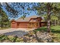 View of the rear exterior showcasing a large garage, stone feature, and lush greenery at 465 Indian Way, Monument, CO 80132