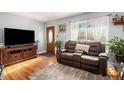 Inviting living room featuring hardwood floors, a leather sofa, natural light, and wood-trimmed front door at 7066 Jennie Dr, Denver, CO 80221