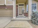 Inviting front entrance with brick accents, covered porch, well-manicured landscaping, and attached garage at 5319 Morning Glory Pl, Highlands Ranch, CO 80130